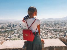 a woman standing on top of a stone wall with a red bag in her hand