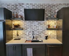 a kitchen with brick wall and white counter tops, black cabinets and dark wood floors