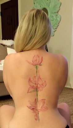 a woman is sitting on the floor with her back turned to the camera and has a pink flower tattooed on her lower back