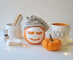 two pumpkins with faces painted on them next to coffee mugs and other items