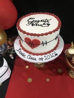 a white and red cake sitting on top of a table next to gold foil balloons