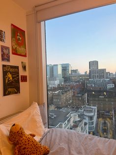 a stuffed animal sitting on top of a bed in front of a window overlooking a city