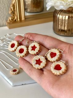 a person is holding five small cookies with red hearts on them and some white flowers in the background