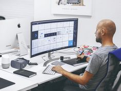 a man sitting in front of a computer monitor on top of a white desk next to a blue chair