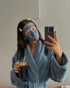 a woman wearing a blue face mask taking a selfie while holding a drink and cell phone