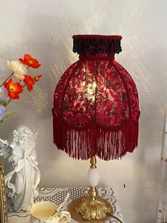 a red table lamp sitting on top of a table next to a vase with flowers