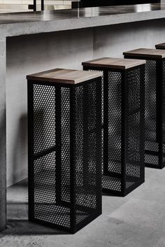 three black metal trash cans sitting next to each other on a concrete floor near a wall