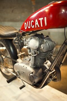 a red motorcycle parked in a garage next to a wooden platform with the word ducati on it