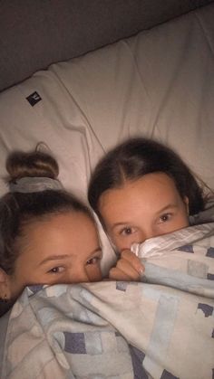 two girls wrapped up in blankets on a bed