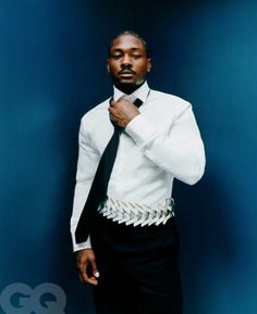 a man in a white shirt and black tie is posing for a photo against a blue wall