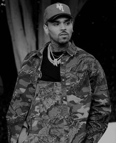 a black and white photo of a young man wearing a camo jacket with a baseball cap