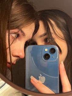 two girls are looking at their cell phones in the mirror while they both look into each other's eyes