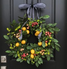 a wreath with oranges and berries hanging on a black front door, next to a light switch