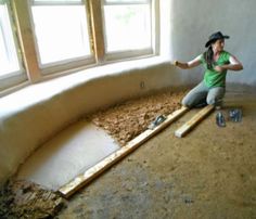 a woman kneeling down on the floor in front of a window with some wood shavings