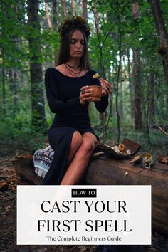 a woman sitting on top of a log in the woods holding a cup and looking at her phone