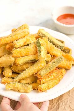 someone is holding a white plate with fried food on it and dipping sauce in the background