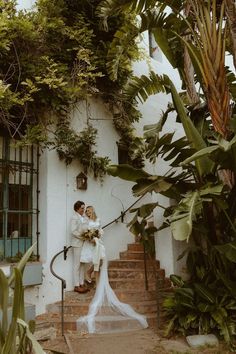 a bride and groom standing on the steps of a house with greenery around them