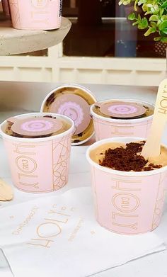 pink cups filled with dirt sitting on top of a table next to wooden spoons