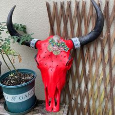 a red cow skull with flowers on it's head sitting next to a fence