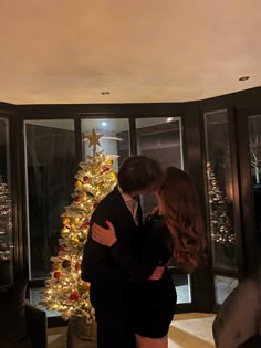 a man and woman embracing in front of a christmas tree