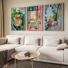 three paintings hang on the wall above a white couch and coffee table in a living room