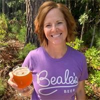 a woman in a purple shirt holding a glass of beer and smiling at the camera