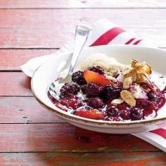 a bowl filled with fruit and ice cream on top of a wooden table next to a fork