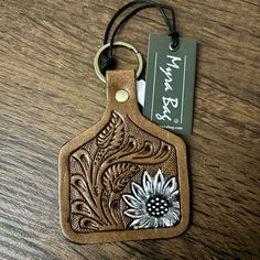 a brown leather keychain with a flower design on the front and an id tag attached to it