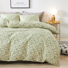 a bed with green and white flowers on it in a room next to a lamp