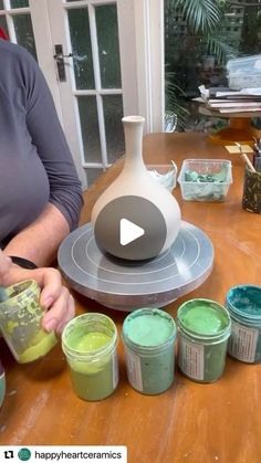 a woman is mixing green paint on a table with several jars and containers in front of her