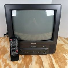 an old television sitting on top of a wooden table with a remote control next to it