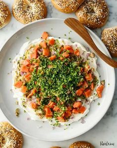 a white plate topped with bagels covered in toppings next to a wooden spoon