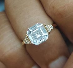 a close up of a person's hand holding a ring with an emerald stone