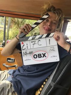 a young man holding up a clapper in the back of a car with his tongue hanging out