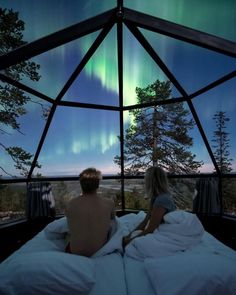 two people sitting on a bed looking at the northern lights