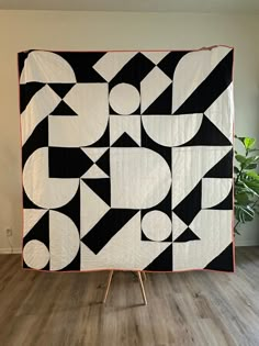 a large black and white quilt sitting on top of a wooden floor next to a potted plant