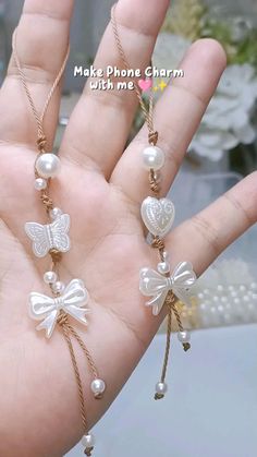 the hand is holding two necklaces with pearls and bows on them, one has a butterfly