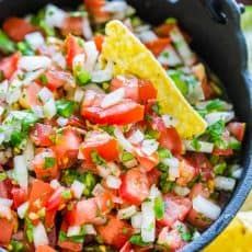 a skillet filled with salsa, tortilla chips and lime wedges on the side