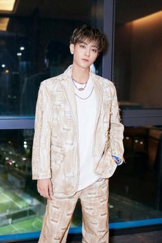 a young man standing in front of a window wearing a white shirt and beige suit