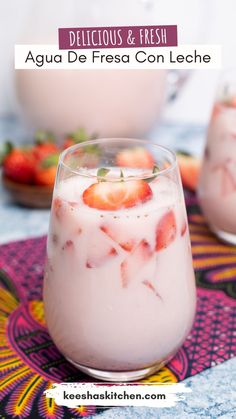 two glasses filled with yogurt and strawberries on a colorful place mat next to another glass full of yogurt