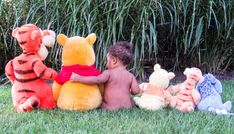 a little boy sitting in the grass with stuffed animals around him and winnie the pooh on his back