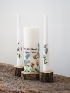 three white candles with blue and orange flowers on them