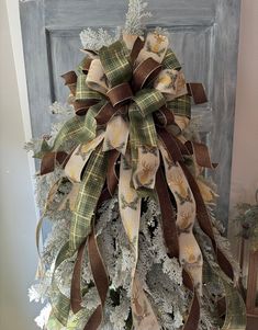 a decorated christmas tree in front of a gray door with brown and white ribbons on it