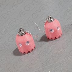 two pink monster shaped earrings are on a gray surface