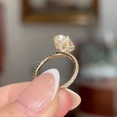 a woman's hand holding an engagement ring in front of her face, with the diamond