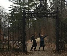 two people standing in front of an iron gate with their arms up and one person reaching for the frisbee