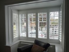 an empty living room with white shutters and black leather chair in front of the window