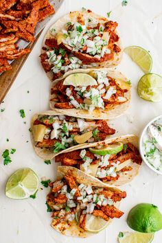 four tacos with meat, onions and cilantro on a white surface next to limes