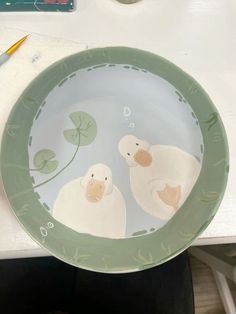 a plate with two ducks on it sitting on a table next to markers and pens