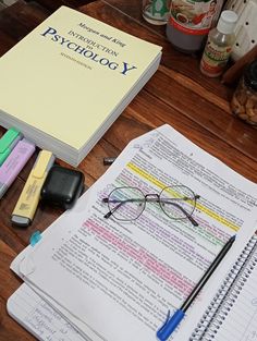 an open book with glasses on top of it next to pens, markers and pencils